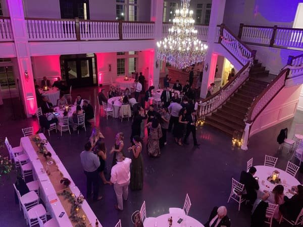 Wedding guests dancing under purple and green uplighting at The Springs in Weatherford, with the DJ booth and bride visible in the reception ballroom.